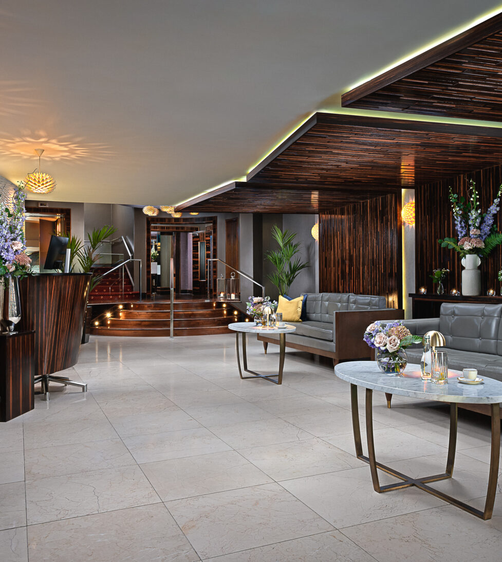 Elegant hotel lobby with cosy seating, modern decor, ambient lighting, floral arrangements, and check-in desks.