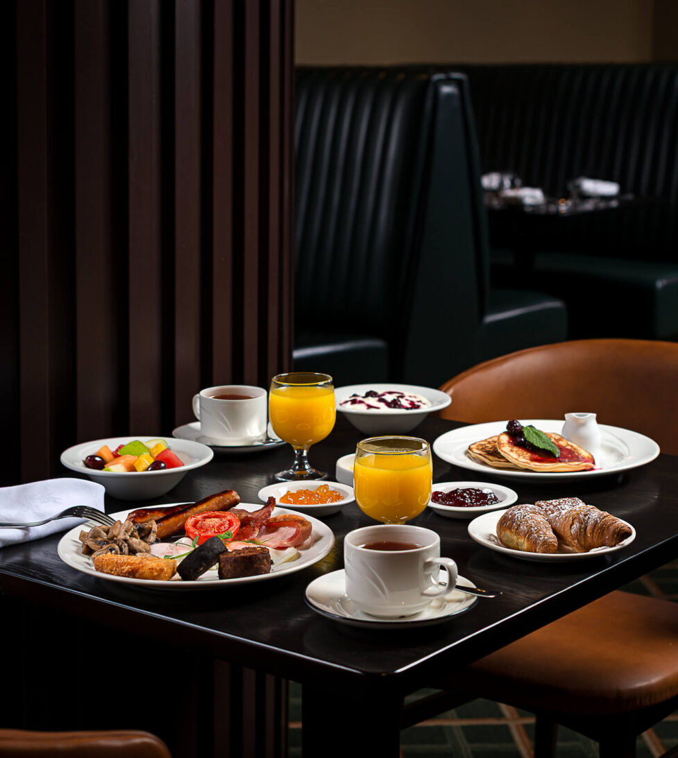 Cosy hotel dining with full English breakfast, fresh fruit, pastries, and orange juice in an elegant seating area.