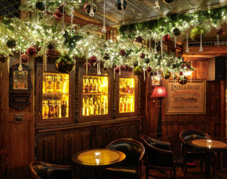 Cosy hotel bar with festive decor, glowing lights, plush seating, and a display of fine whiskies for a warm, inviting atmosphere.