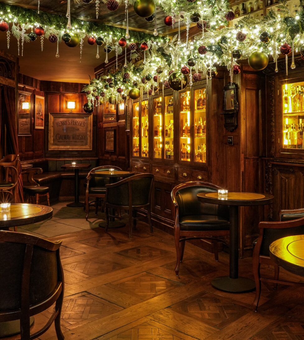 Cosy hotel bar with warm lighting, festive garlands, wooden furniture, and a well-stocked drinks cabinet.