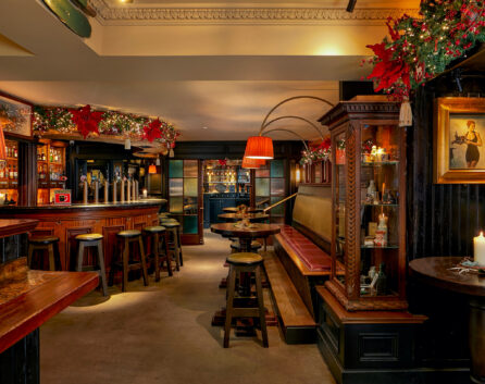 Cosy hotel bar with festive decor, warm lighting, wooden stools, and elegant paintings, perfect for a relaxing evening.