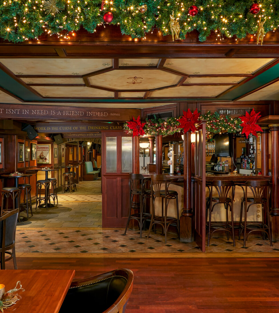 Warm hotel pub with festive decor, cosy seating, wood panelling, and ambient lighting, perfect for a relaxed evening.
