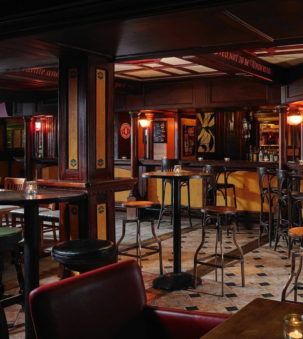 Cosy hotel pub with warm lighting, elegant wooden décor, high stools, and inviting ambiance for relaxing evenings.