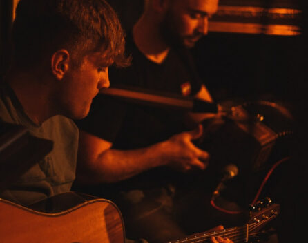 Live folk band playing guitar and accordion in cosy hotel lounge with warm lighting, inviting atmosphere for guests.