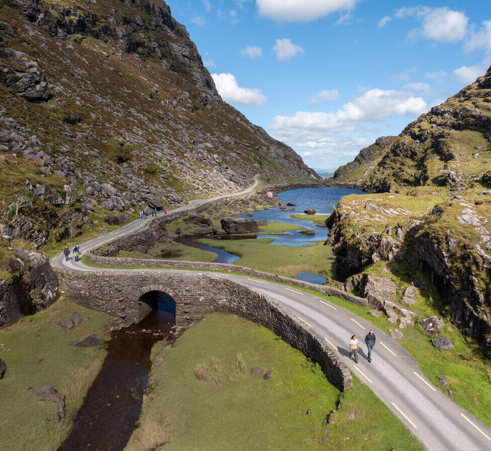 Guests enjoying a scenic walk along a stone bridge amidst lush hills and serene waters, capturing Ireland's natural beauty.