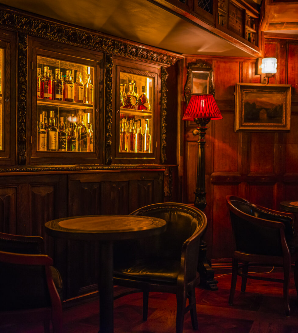 Cozy hotel pub with vintage decor, plush leather chairs, wooden tables, warm lighting, and a well-stocked bar.