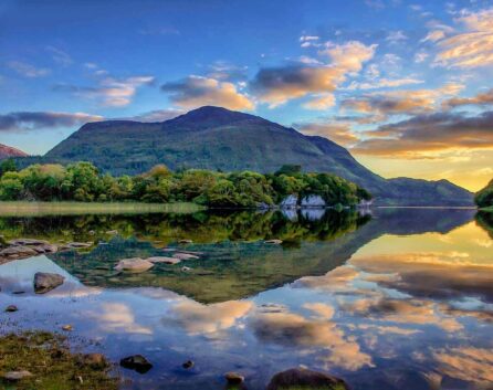 Serene lake with mountain reflection, lush greenery, and vibrant sunset skies, inviting relaxation and nature exploration.