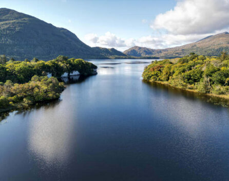 Serene lakeside view with lush green hills, reflecting tranquil atmosphere, ideal for relaxation and scenic exploration.