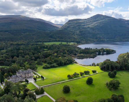 Majestic countryside hotel surrounded by lush greenery, nestled beside a serene lake with mountain views and vast open spaces.