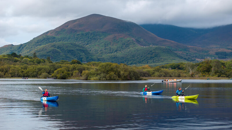 Guests kayaking on a serene lake with lush mountains in the background, enjoying outdoor adventure and scenic views.