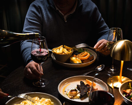 Guest enjoying gourmet dinner with wine, featuring steak and chips in elegant hotel restaurant ambiance.