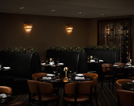 Elegant hotel dining room with cosy booths, warm lighting, festive garlands, and luxurious table settings.
