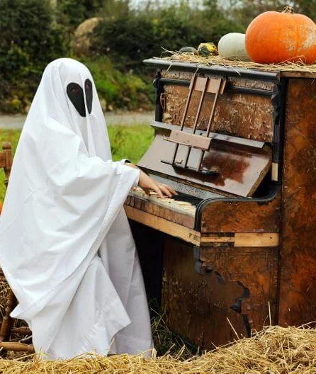 Ghostly figure playing an old piano in a pumpkin-filled field, surrounded by autumn hay bales, creating a whimsical, spooky scene.