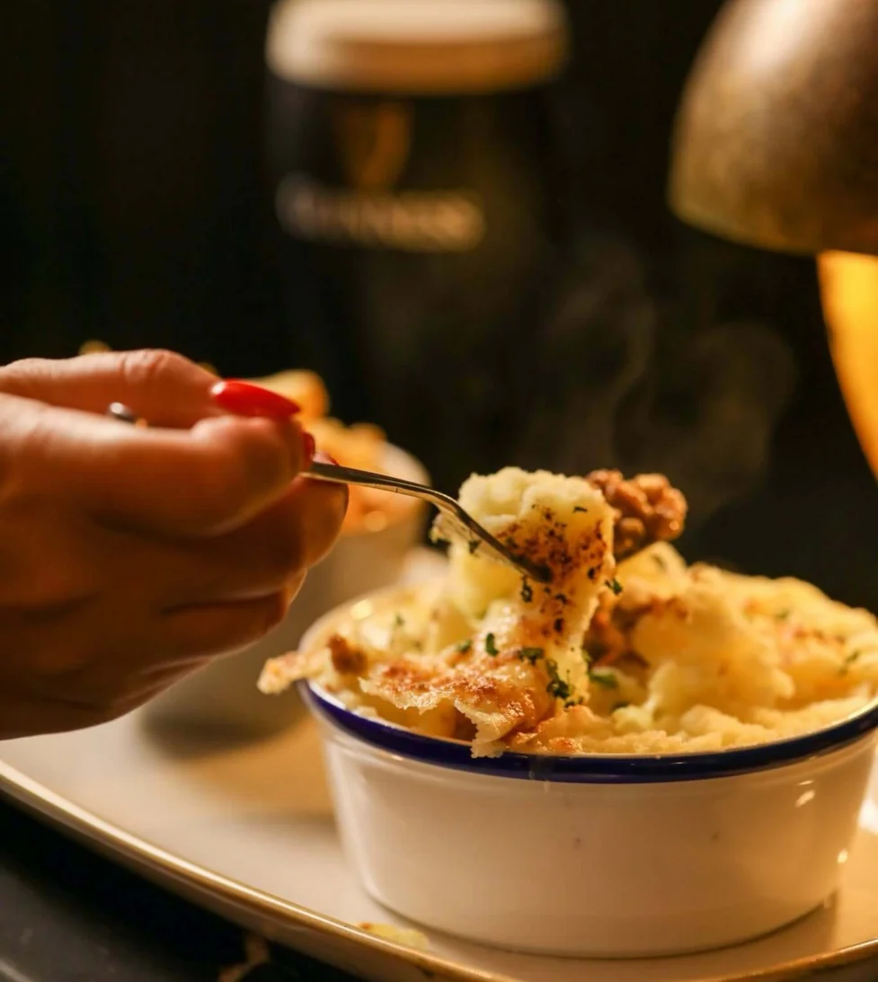Guest enjoying hearty cottage pie with a pint in cosy hotel restaurant, featuring warm lighting and inviting atmosphere.