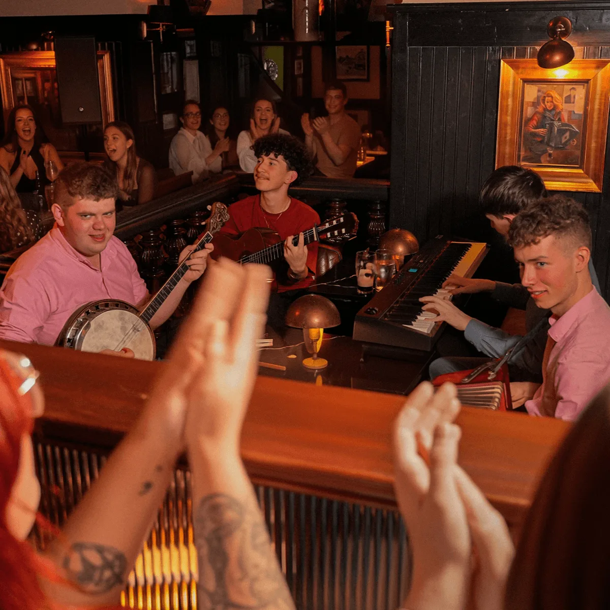 Lively hotel pub session with live band (banjo, guitar, keyboard), guests clapping, warm wooden interior and cosy table lamps.