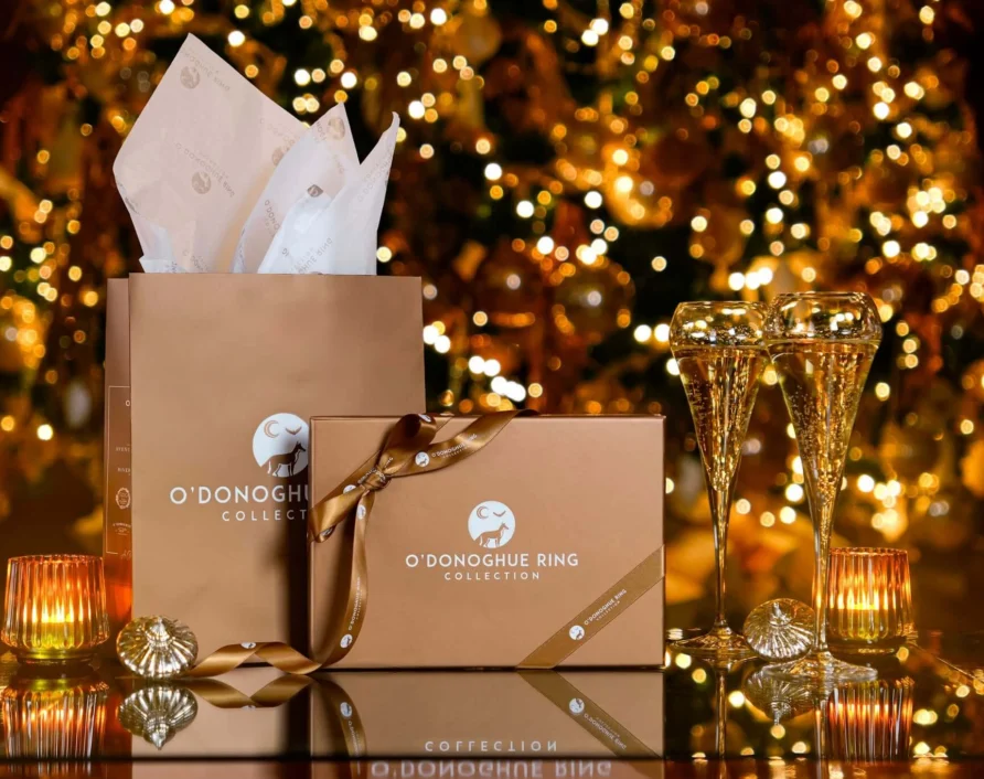 Festive hotel gift boxes, ribbon and tissue with sparkling Christmas tree lights and two champagne flutes by candlelight