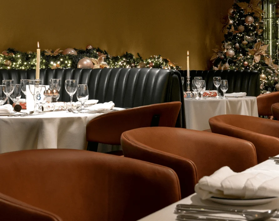 Festive hotel restaurant with leather banquettes, candlelit tables, glassware set for dinner and decorated Christmas tree — cosy dining and seasonal ambiance